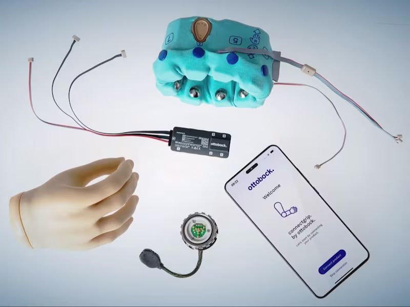 An assortment of Ottobock products scatted about, including the speedhand myoelectric prosthetic hand, the myosmart cuff prosthetic device, and a phone displaying the connectgrip app.
