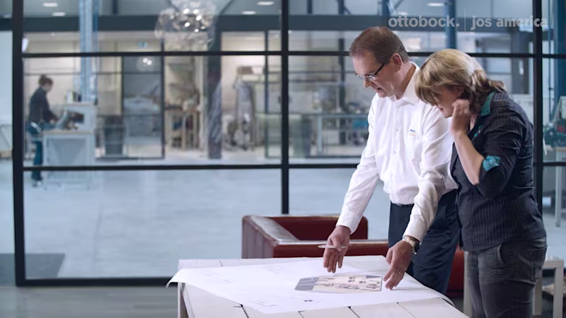 Team reviewing prosthetic design blueprints in Ottobock industrial workspace.