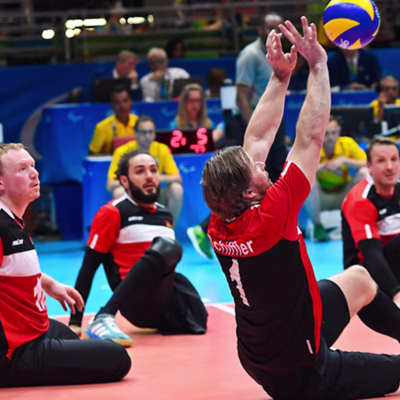 A team of amputated volleyball players watch intently as their teammate reaches for the ball