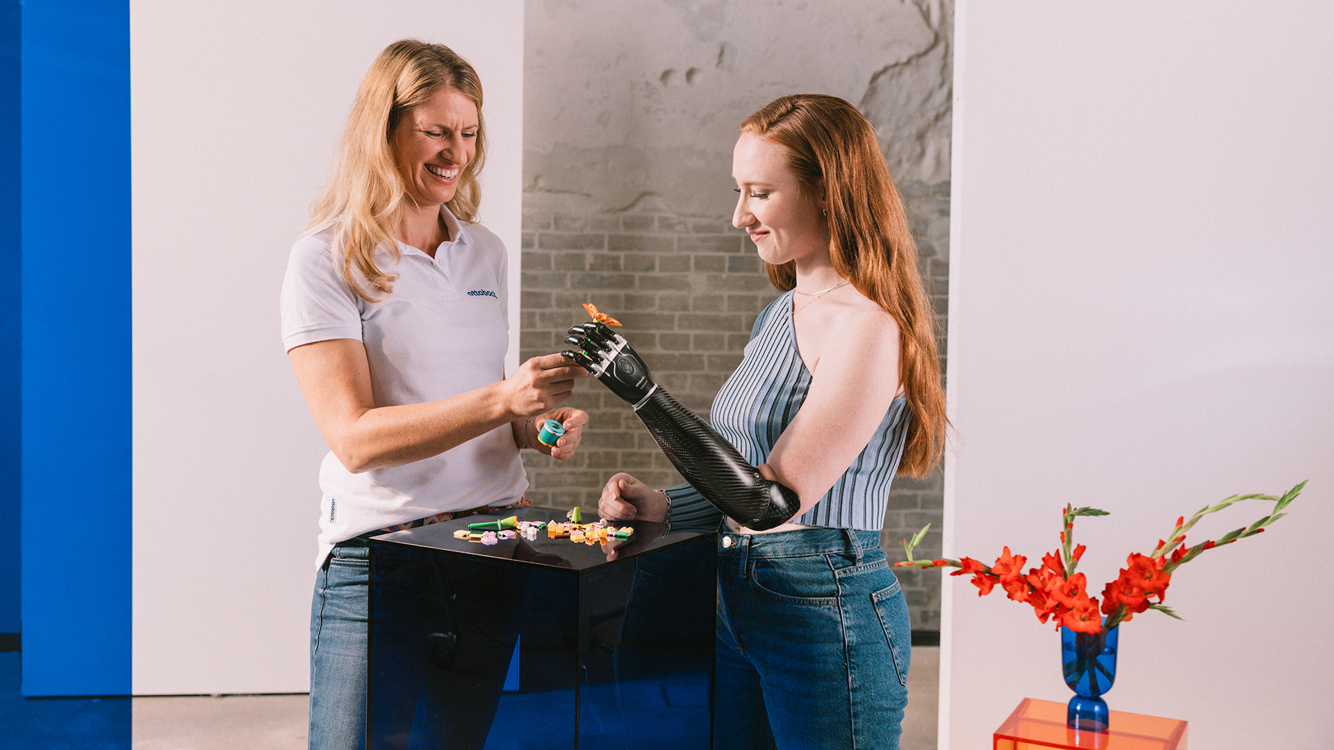 a bebionic prosthetic hand user takes an orange Lego flower from her prosthetist. 
