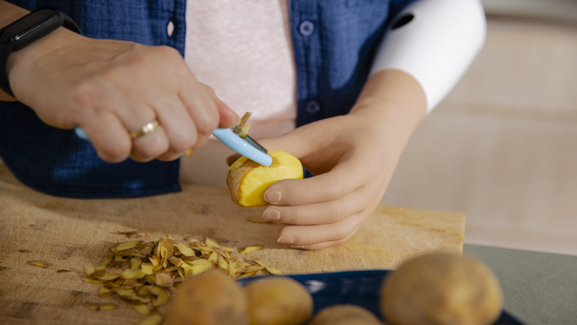 Ottobock prosthetic hand user peeling potatoes in the kitchen.