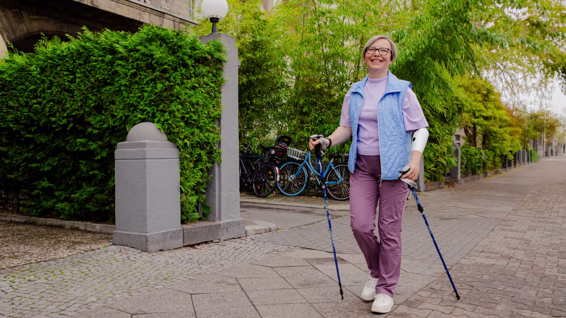 Prosthetic hand user practicing Scandinavian walking with poles outdoors.