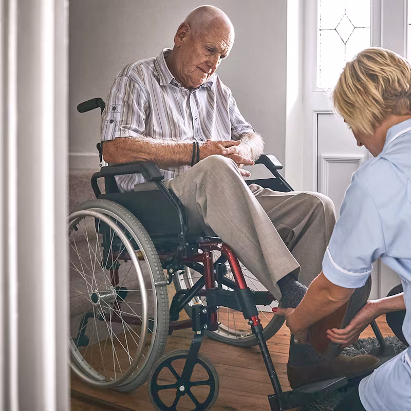 Eine Frau hilft einem im Rollstuhl sitzenden Mann bei der Positionierung seines Fußes.