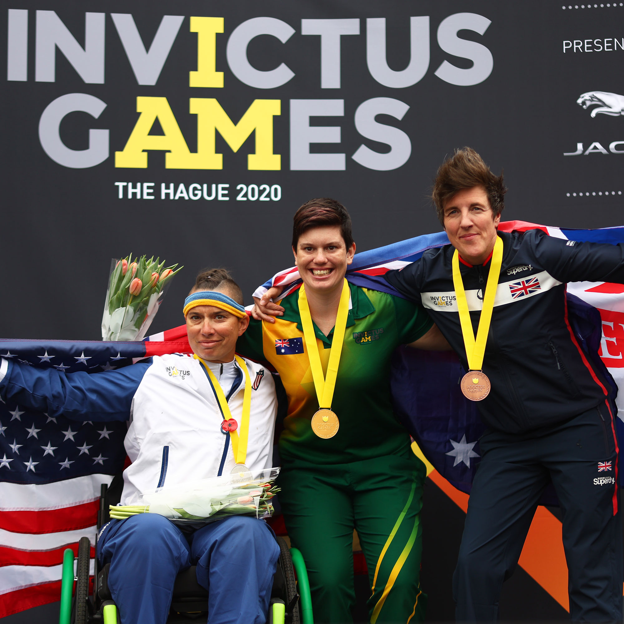 Trois athlètes vétérans aux Jeux Invictus posent avec leurs médailles et leurs drapeaux nationaux.