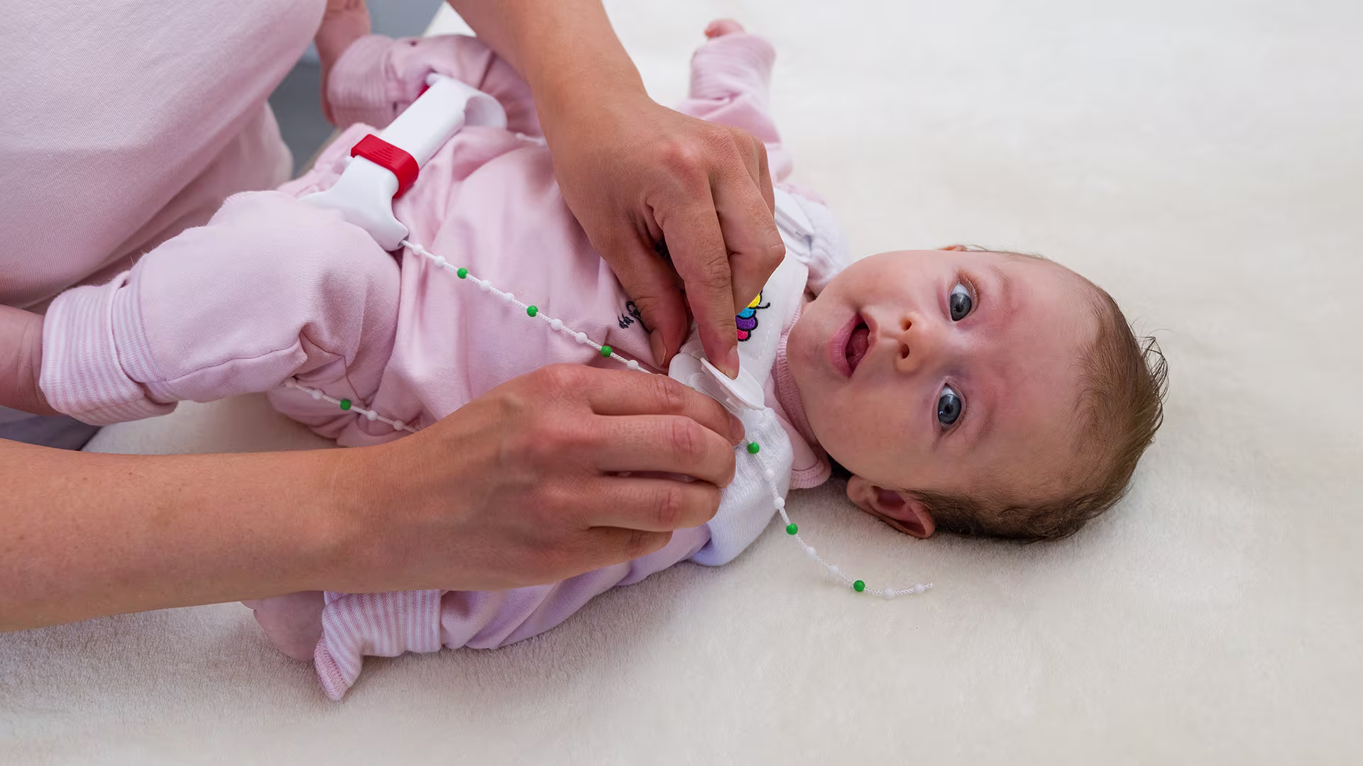 Ein Baby liegt auf einem Wickeltisch, die Mutter zieht dem Kind die Tübinger Hüftbeugeschiene von Ottobock an.