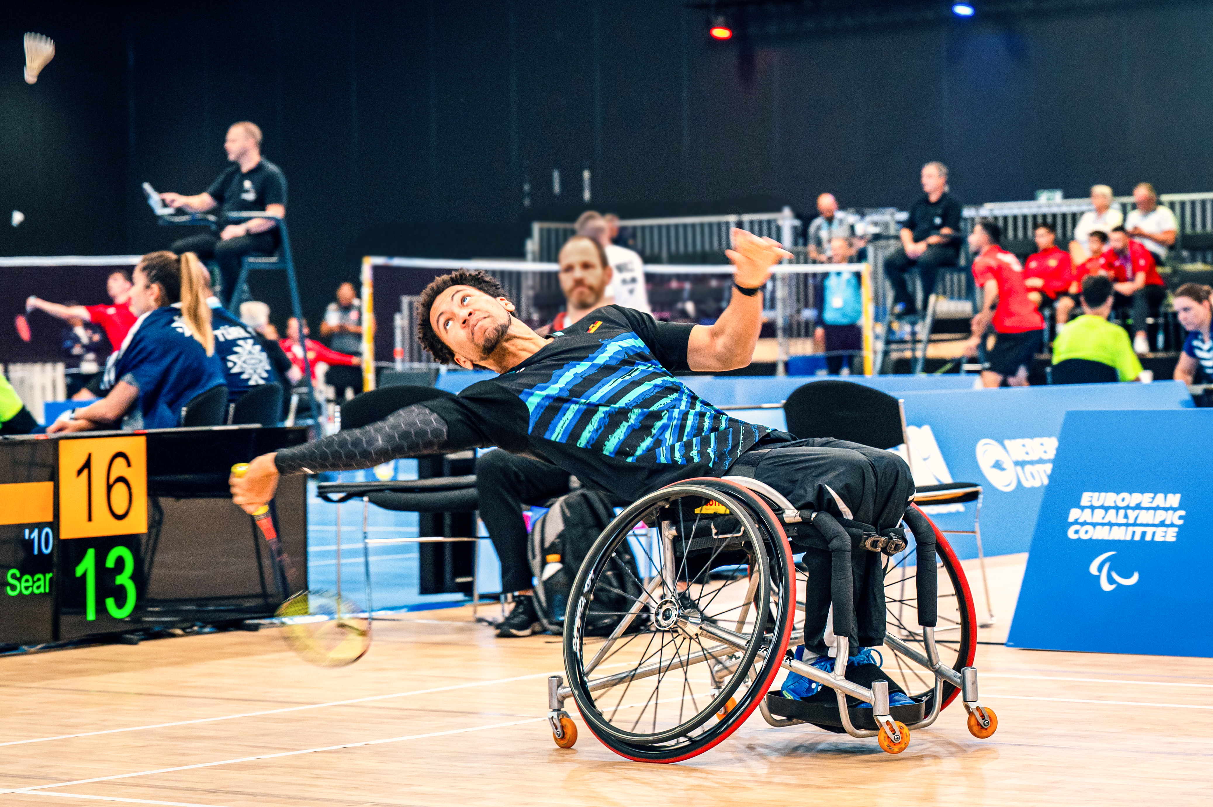 Wheelchair badminton player in the Ottobock Invader sports wheelchair reaches far back to catch a flying badminton ball