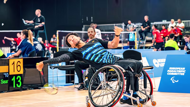 Wheelchair badminton player in the Ottobock Invader sports wheelchair reaches far back to catch a flying badminton ball