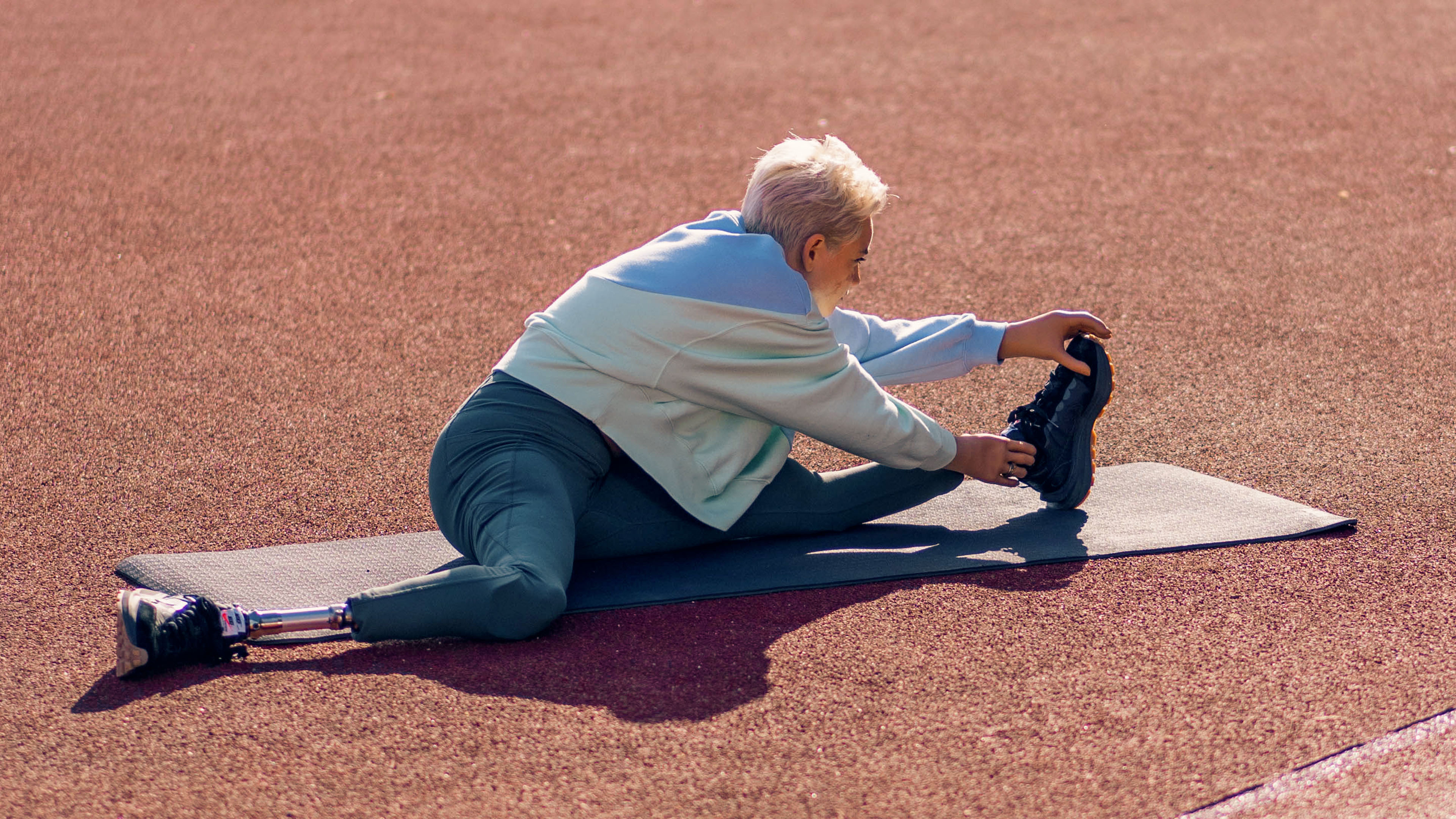 Ottobock bionic hand user, Bebe, stretches her left leg on a yoga mat on a running course
