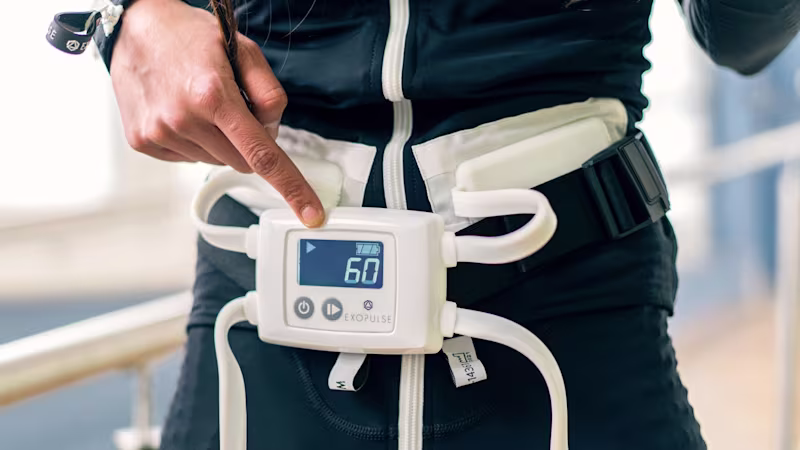 Frau im Ottobock Exopulse Mollii Suit, die die Steuereinheit des Anzugs einschaltet.