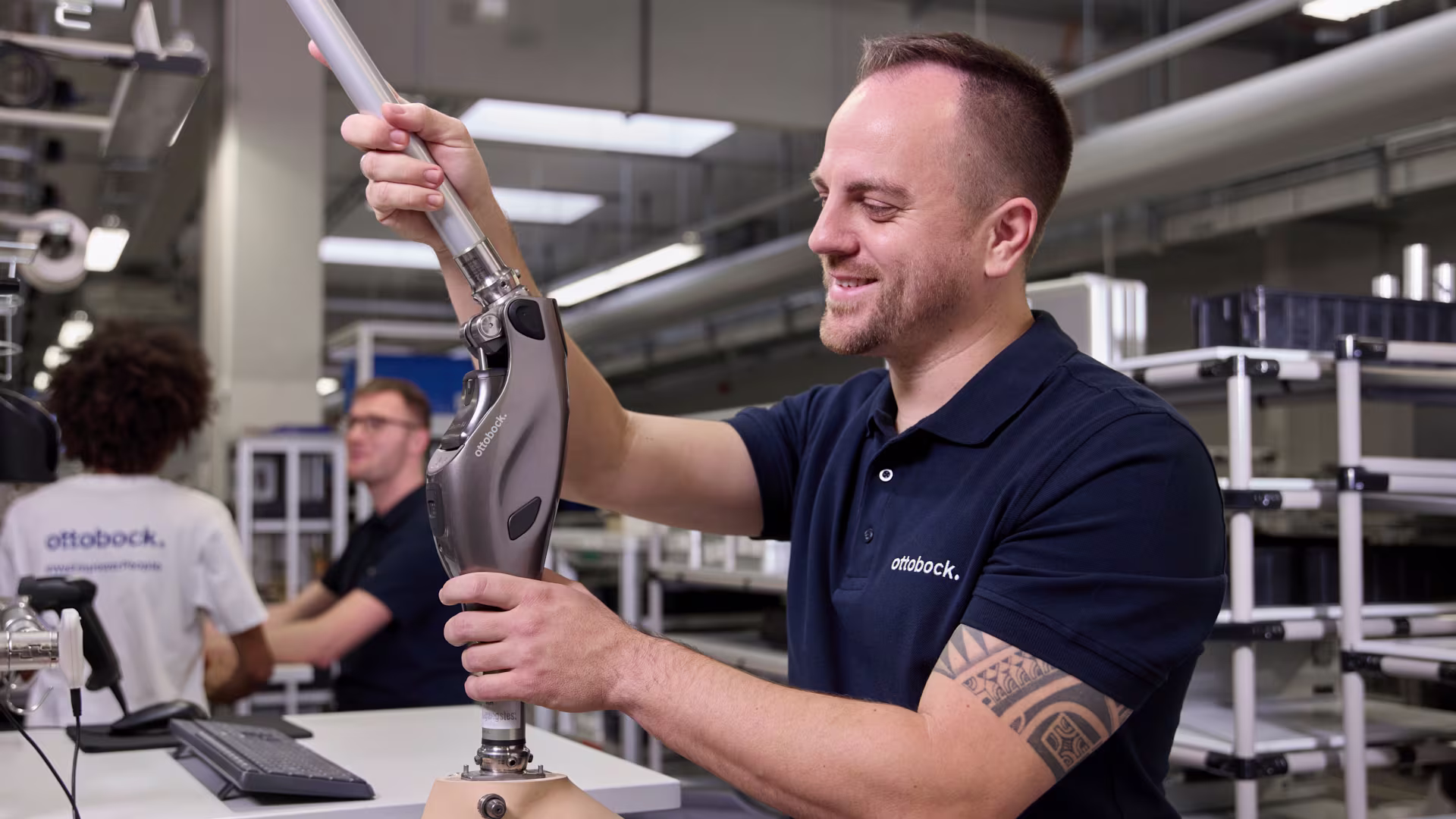 A man is standing at a workbench, holding a prosthetic leg with a Genium X4 in his hands.