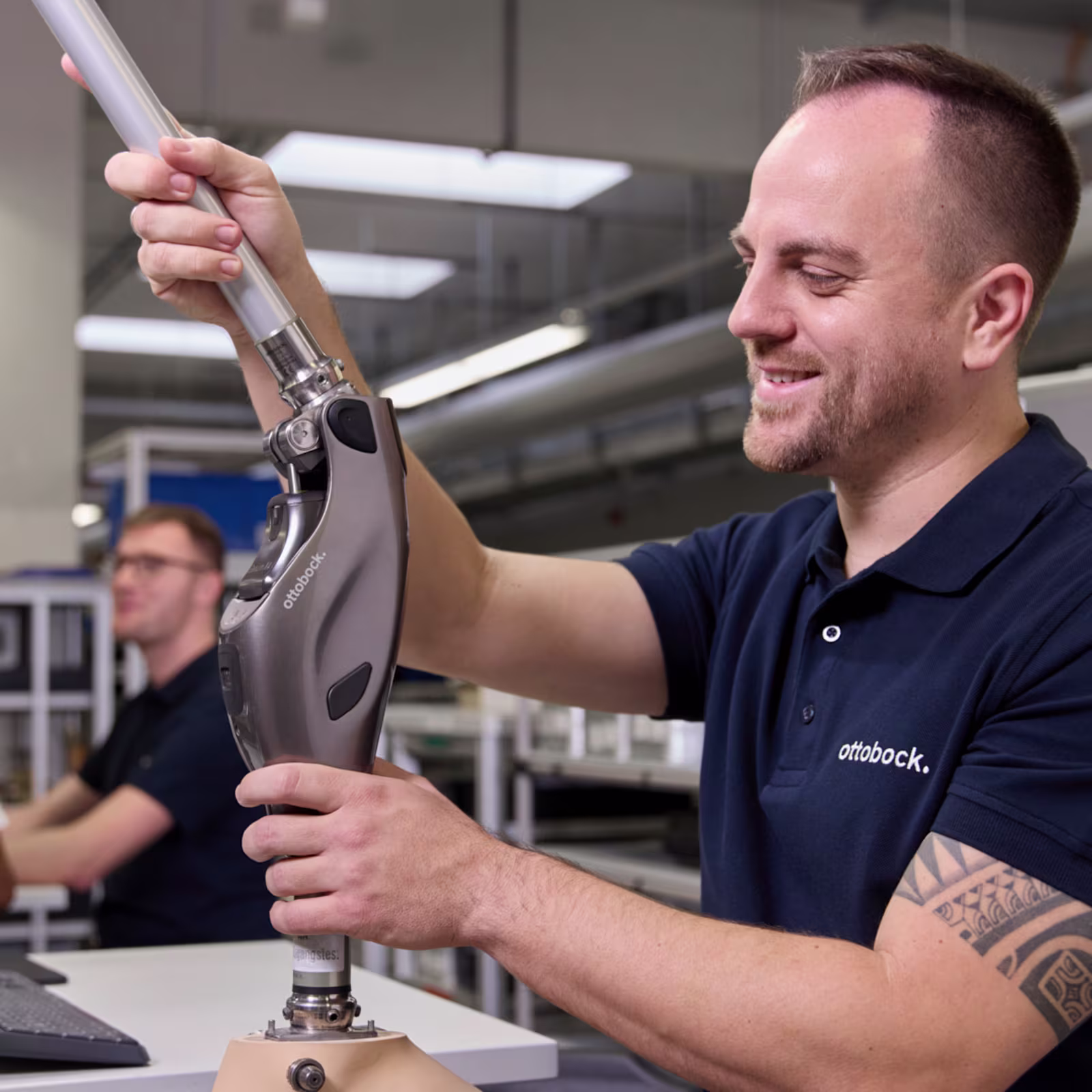 A man is standing at a workbench, holding a prosthetic leg with a Genium X4 in his hands.