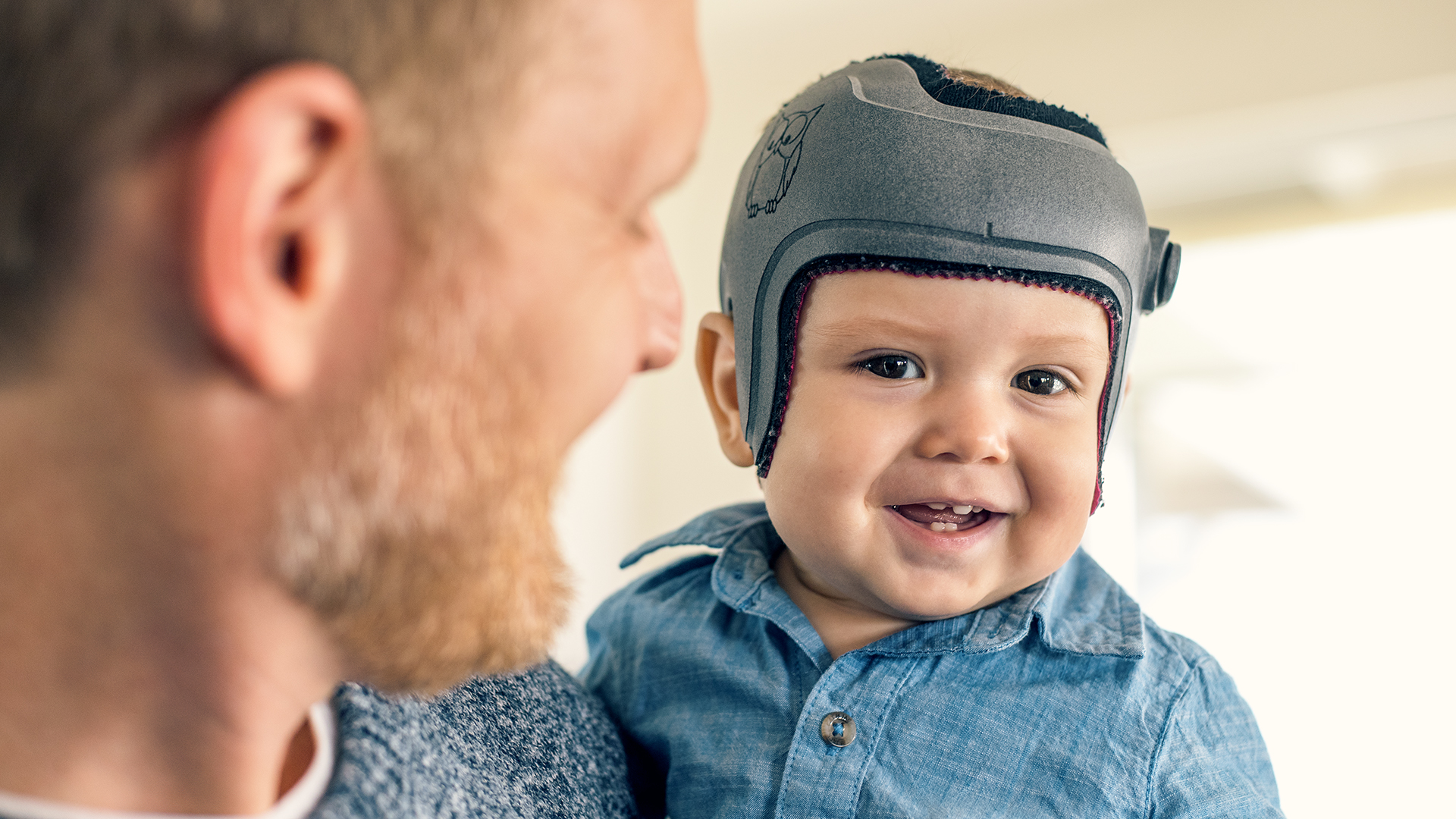 Harrison is wearing the MyCRO Band helmet and smiles on his fathers arm.