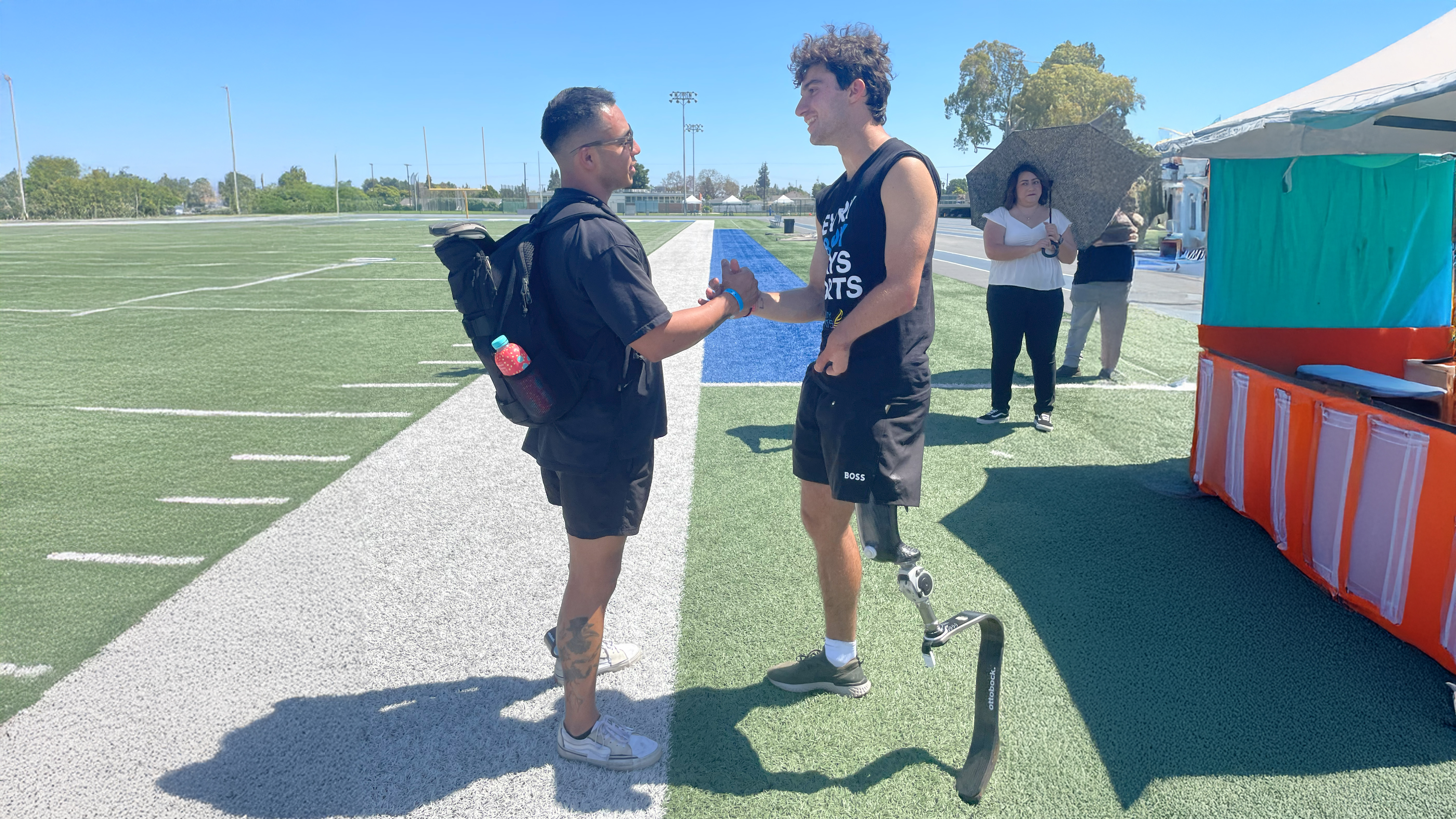 Paralympian Ezra Frech greeting a volunteer on an outdoor field at a Ottobock Running Clinic event