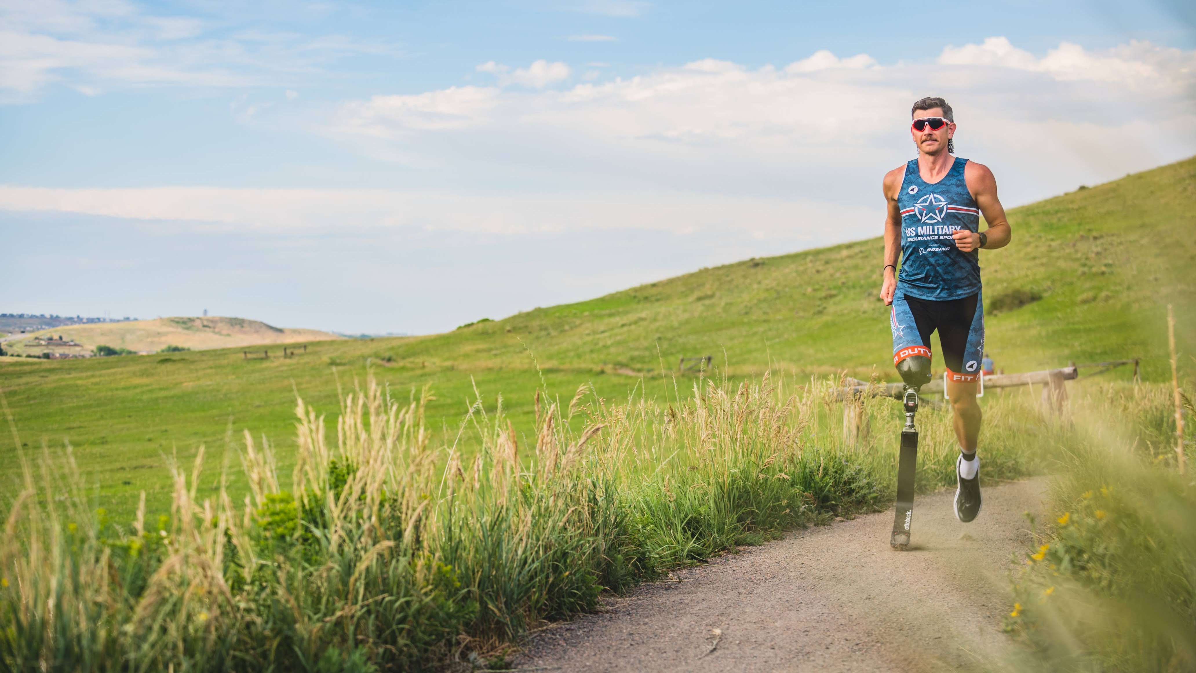 Adam Popp running through an outdoor plain on a course in his running prosthetic blade