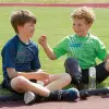 Two young athletes sit on an outdoor racing track with water bottles