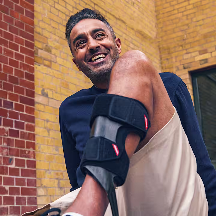 Eine männliche gelesene Person mit dunklen Haaren sitzt auf einer Mauer. Im Fokus des Bildes ist ein rechtes Bein, an dem er eine WalkOn Reaction lateral Orthese trägt.