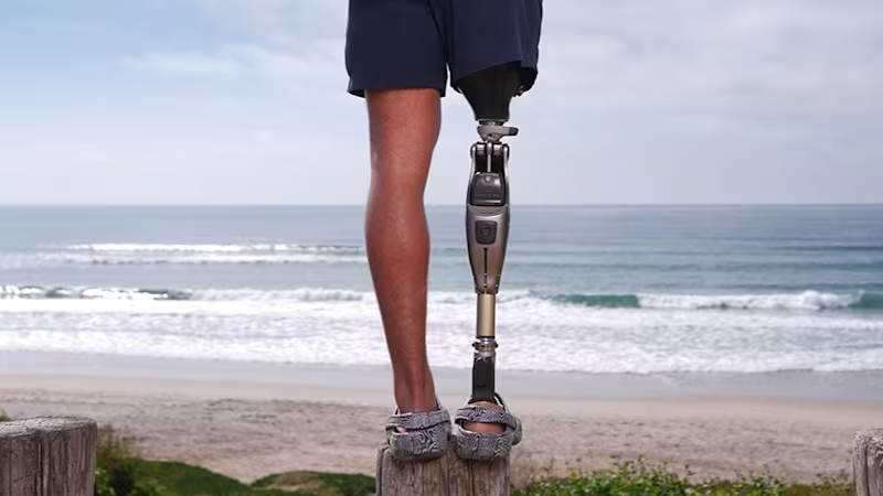 Das Bild zeigt den Unterkörper einer amputierten Person. Am rechten Bein trägt die Person das mechatronische Prothesenkniegelenk Genium X4 von Ottobock. Im Hintergrund sind Strand und Meer zu sehen.