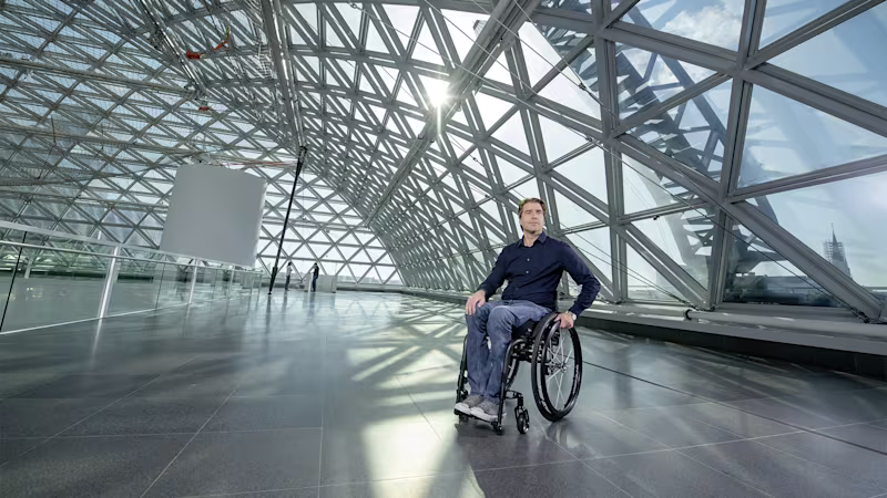 A man in an Ottobock wheelchair in a large empty hall in front of a large glass front