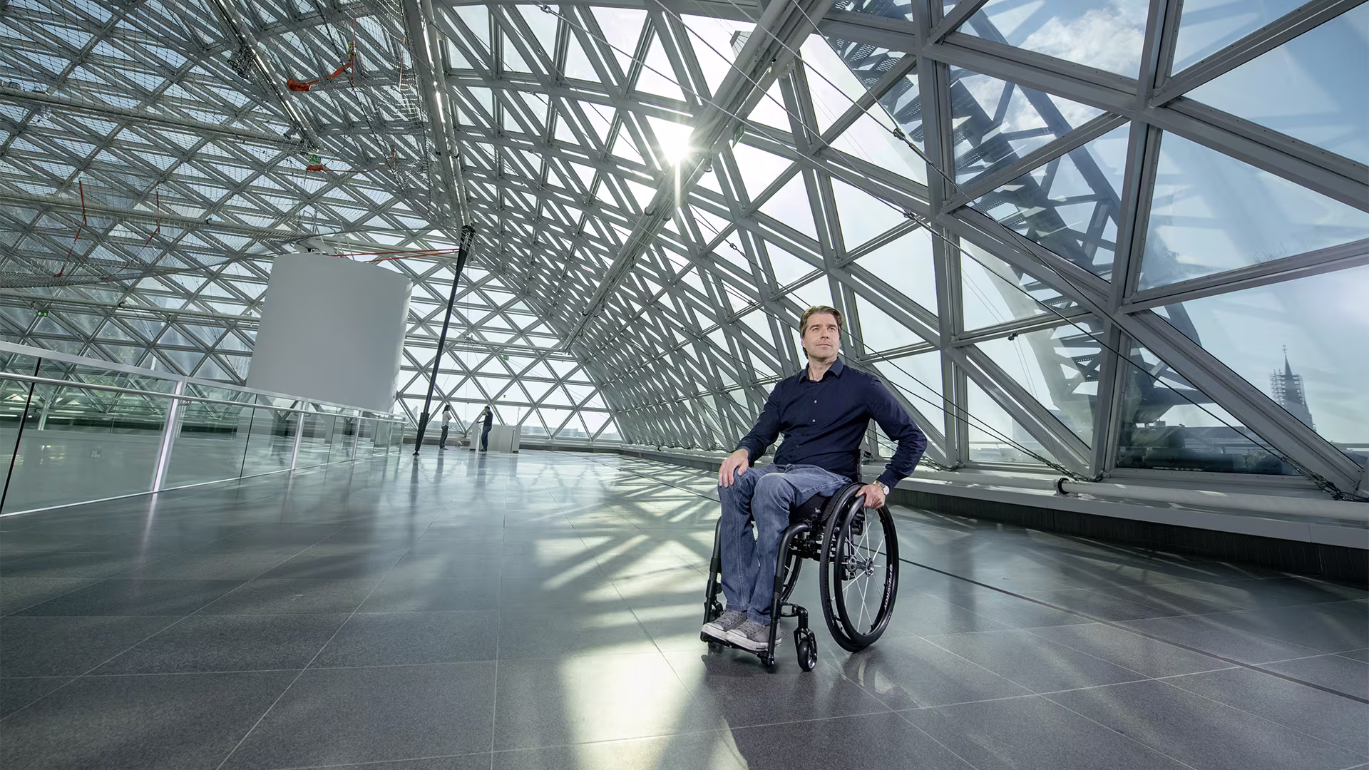 A man in an Ottobock wheelchair in a large empty hall in front of a large glass front