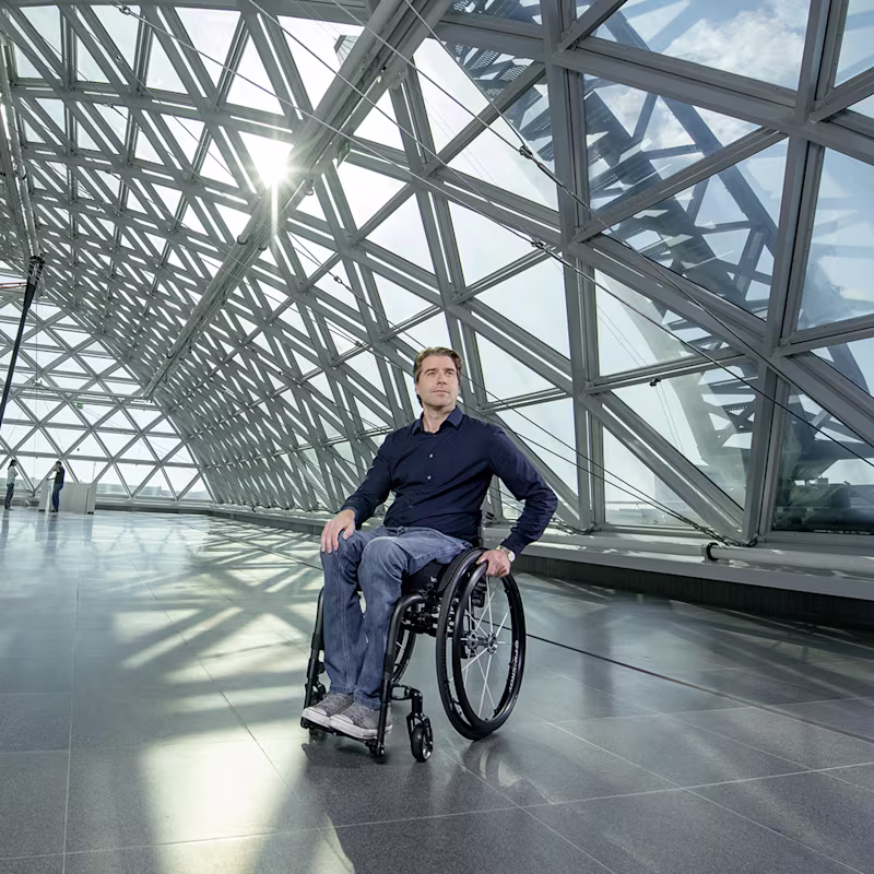 A man in an Ottobock wheelchair in a large empty hall in front of a large glass front