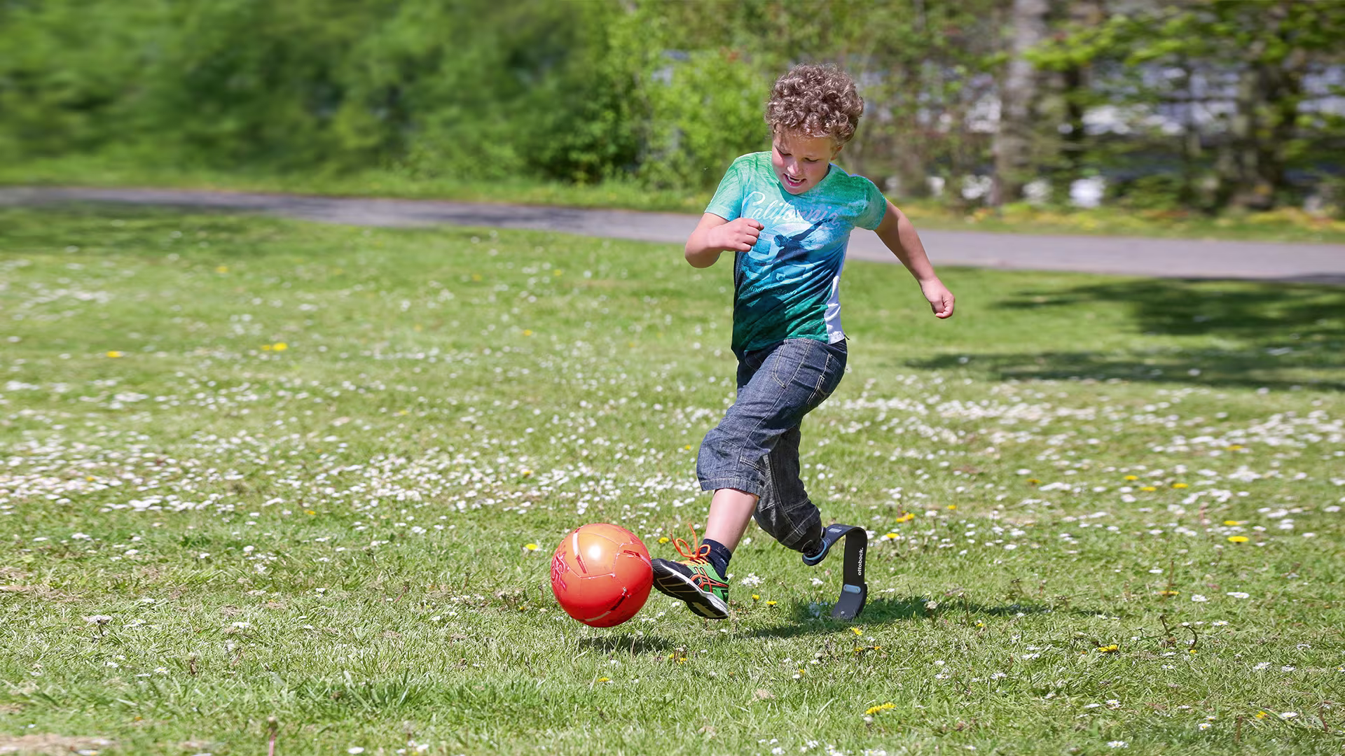 A child with a sports prosthesis plays football in a garden