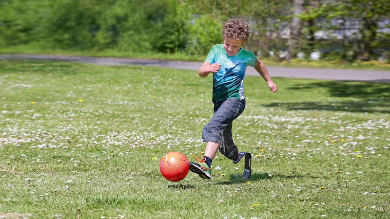 A child with a sports prosthesis plays football in a garden