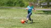 Un enfant avec une prothèse de sport joue au football dans un jardin