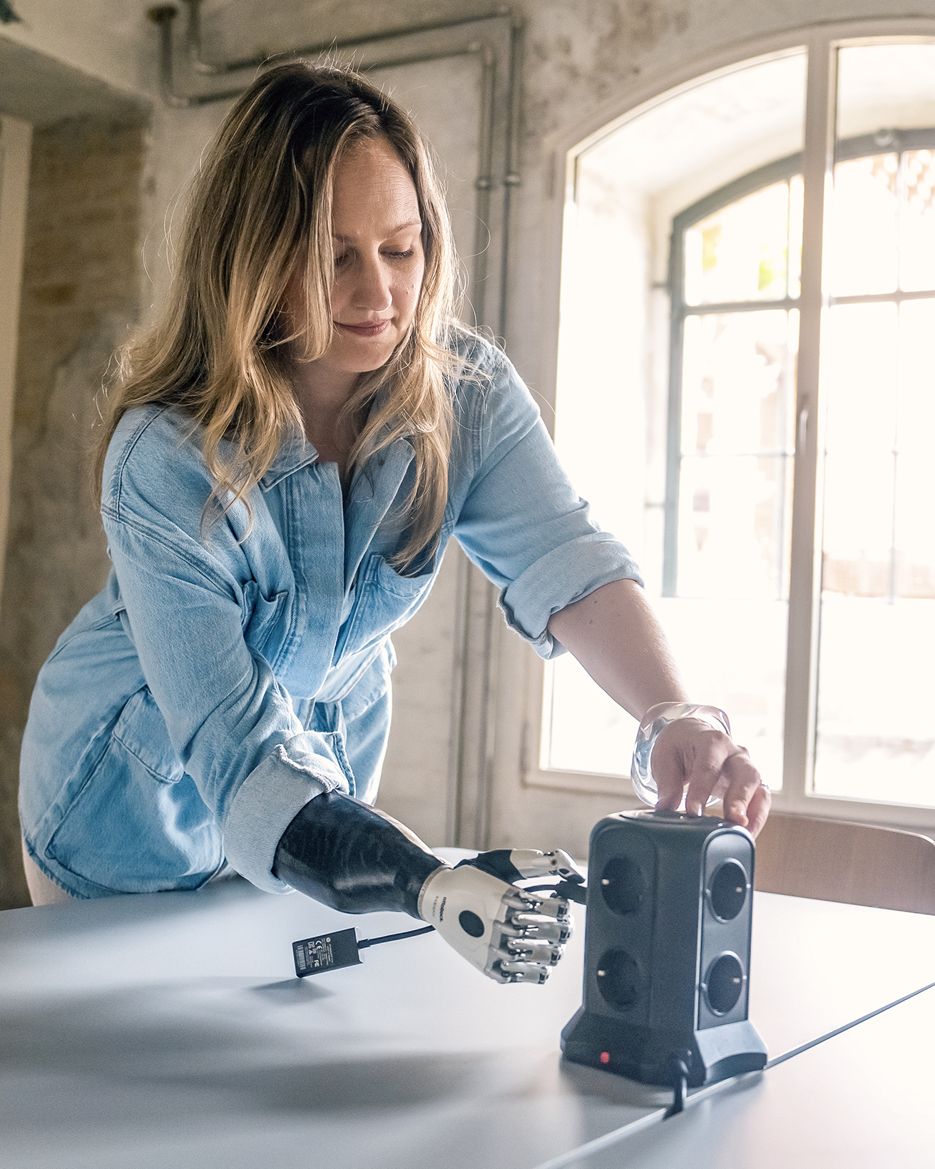Prosthetic arm user Johanna with Ottobock bebionic hand using a power socket in the office.