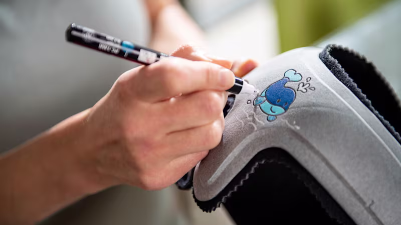 A parent drawing a whale on their child's MyCRO Band cranial helmet