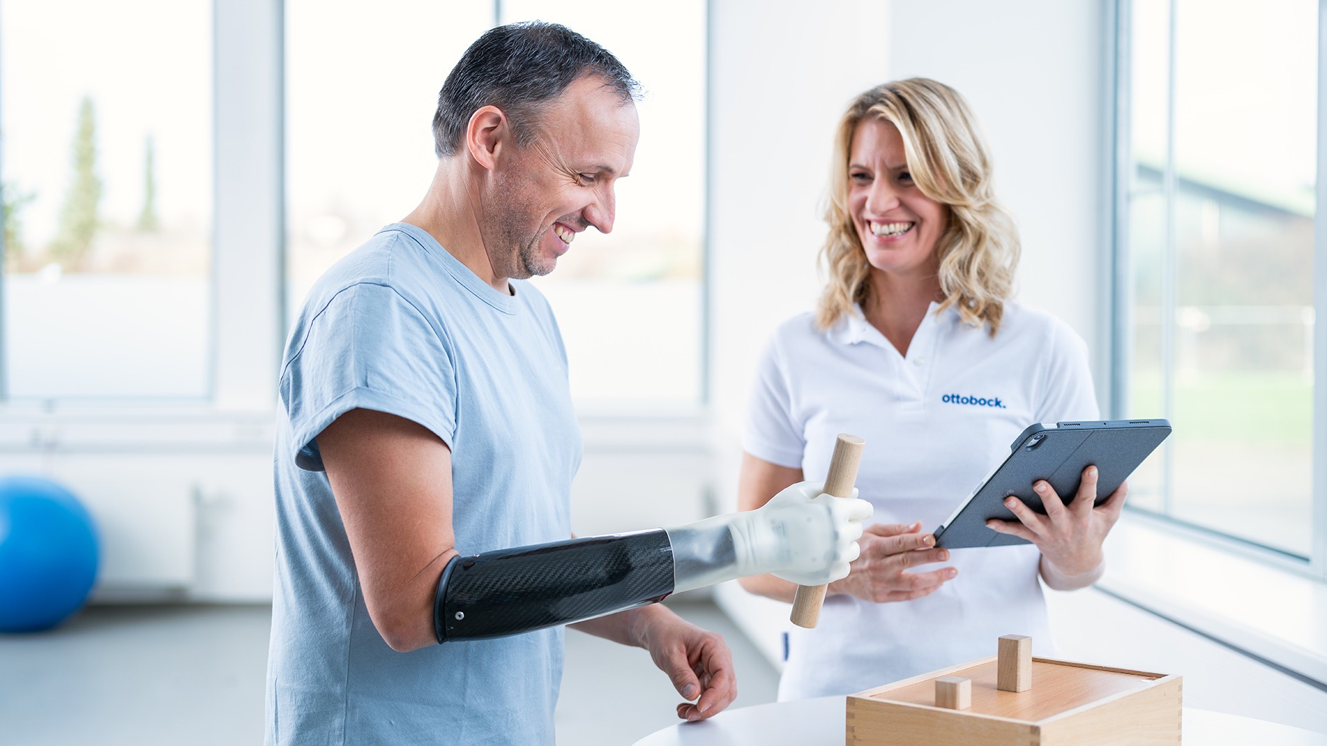 Ein Arm amputierter Mann trägt die michelangelo Hand von Ottobock und übt die Benutzung der Prothese gemeinsam mit einer Therapeutin.