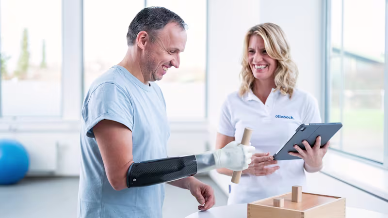 Ein Arm amputierter Mann trägt die michelangelo Hand von Ottobock und übt die Benutzung der Prothese gemeinsam mit einer Therapeutin.