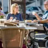 Der Rollstuhlanwender Harald sitzt in einem Wingus von Ottobock in der Stadt im Cafe und trinkt einen Kaffee.