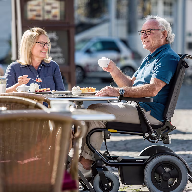Der Rollstuhlanwender Harald sitzt in einem Wingus von Ottobock in der Stadt im Cafe und trinkt einen Kaffee.