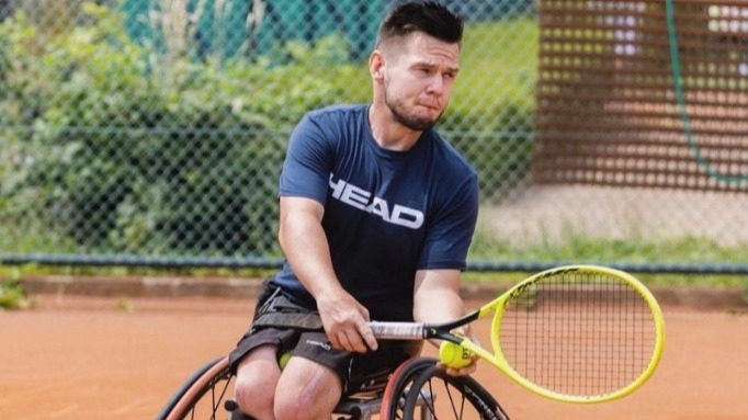 Een jonge man in een rolstoel in beweging met een tennisracket en bal.