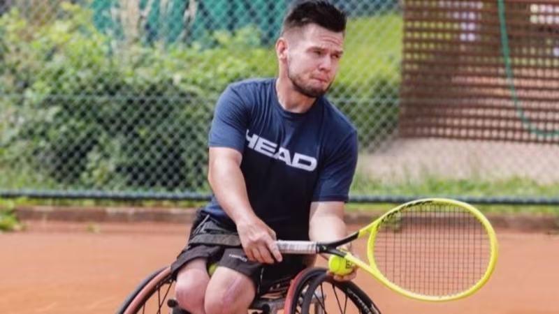 A young man in a wheelchair holding a tennis racket and ball, captured in movement.