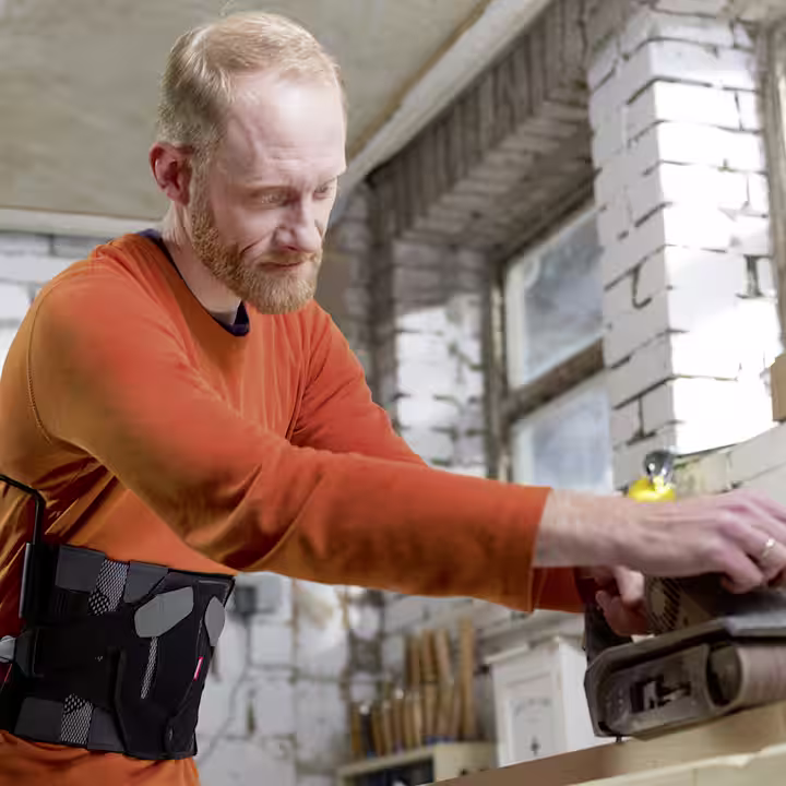 Man wearing a cervical spinal brace using tools in a workshop.