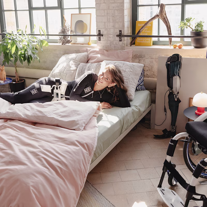 Sina a letto nella sua stanza con la neurotuta Exopulse e C-Brace