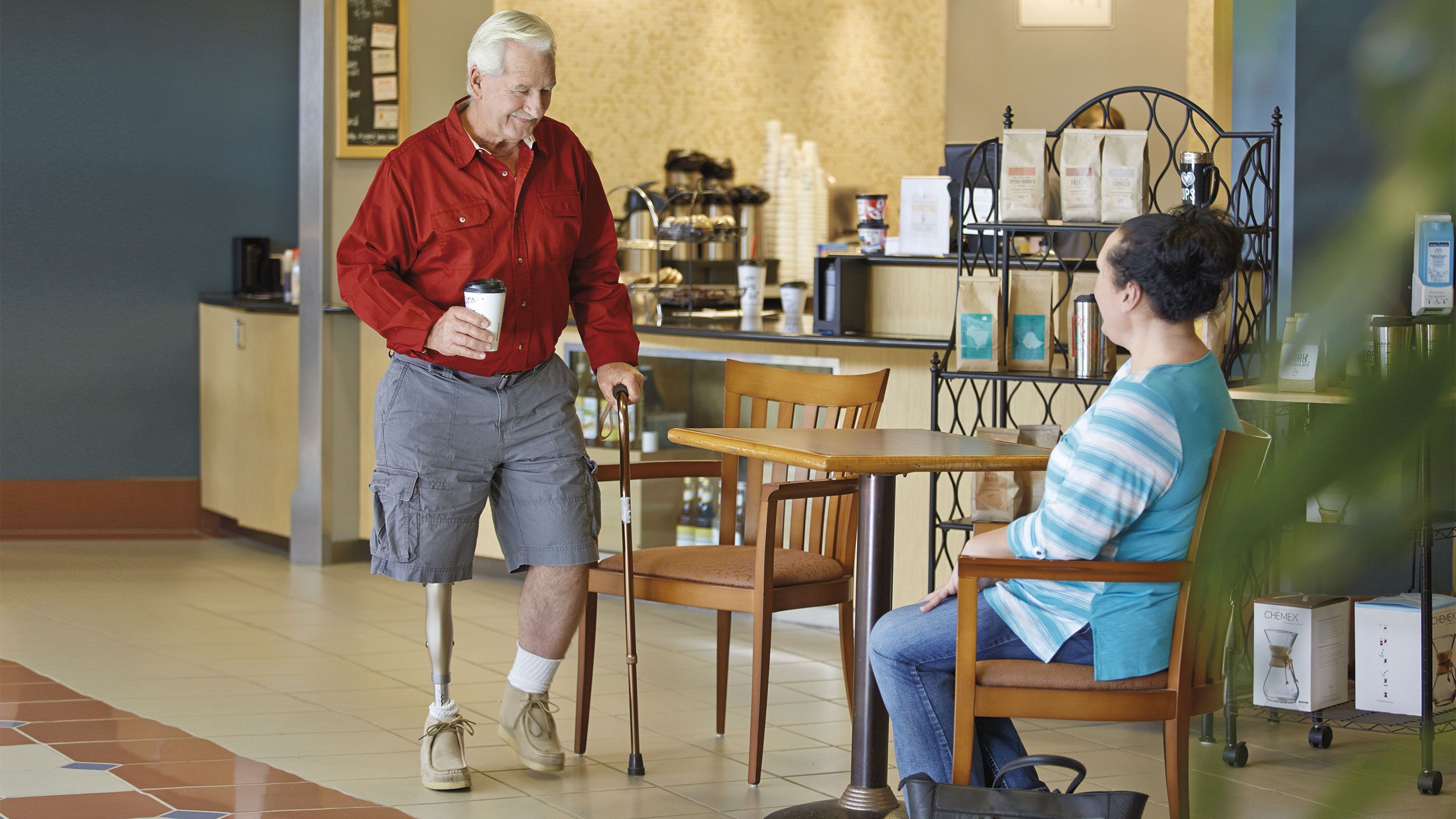 Bob carries a cup of coffee to a café table with his Kenevo Microprocessor Knee.
