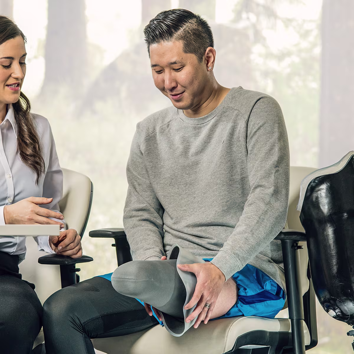 Prosthetist sitting at a table and talking to a leg amputee who shows his residual limb with a liner on