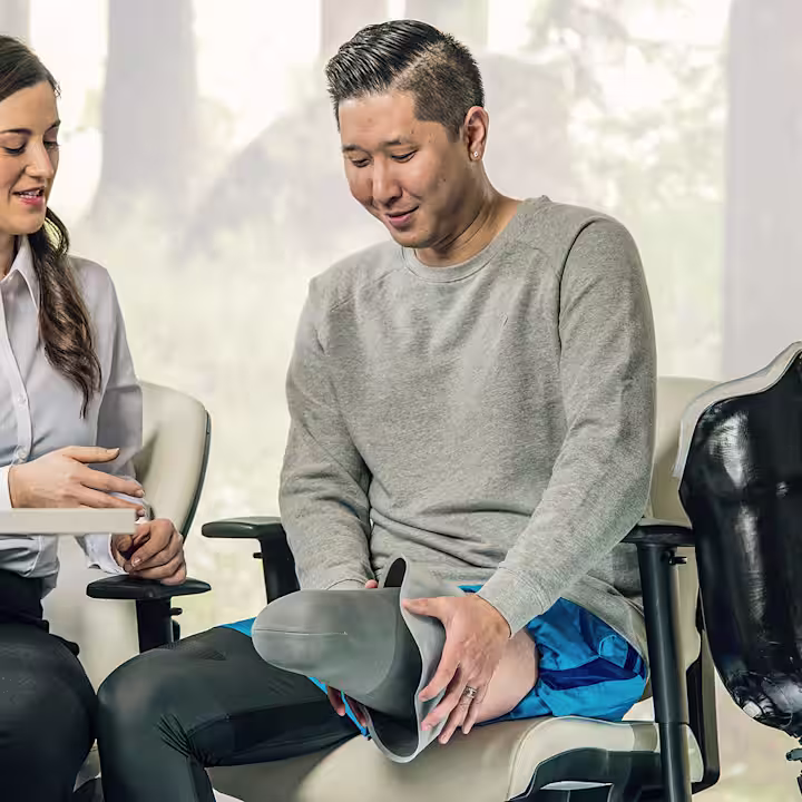 Prosthetist sitting at a table and talking to a leg amputee who shows his residual limb with a liner on