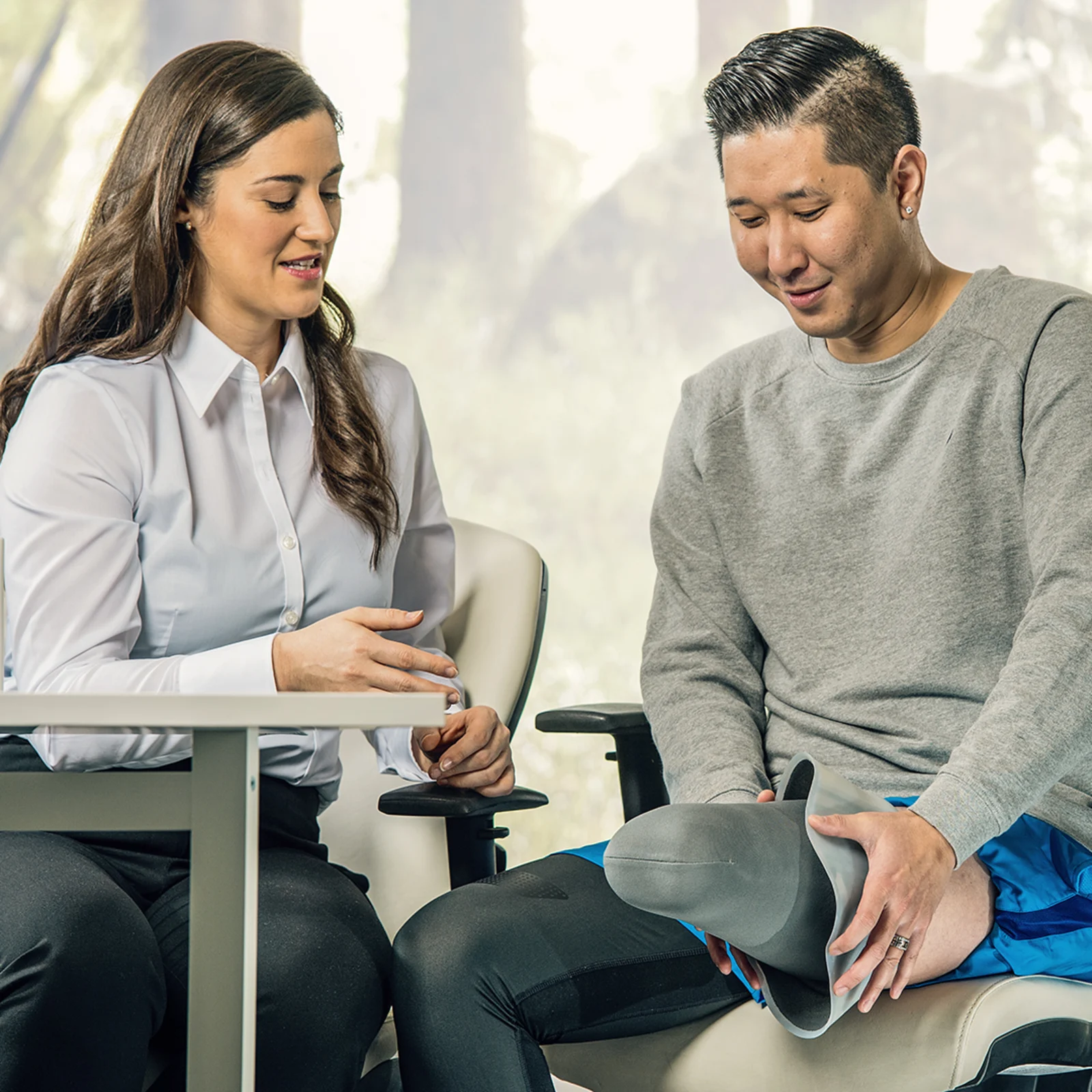 Prosthetist sitting at a table and talking to a leg amputee who shows his residual limb with a liner on