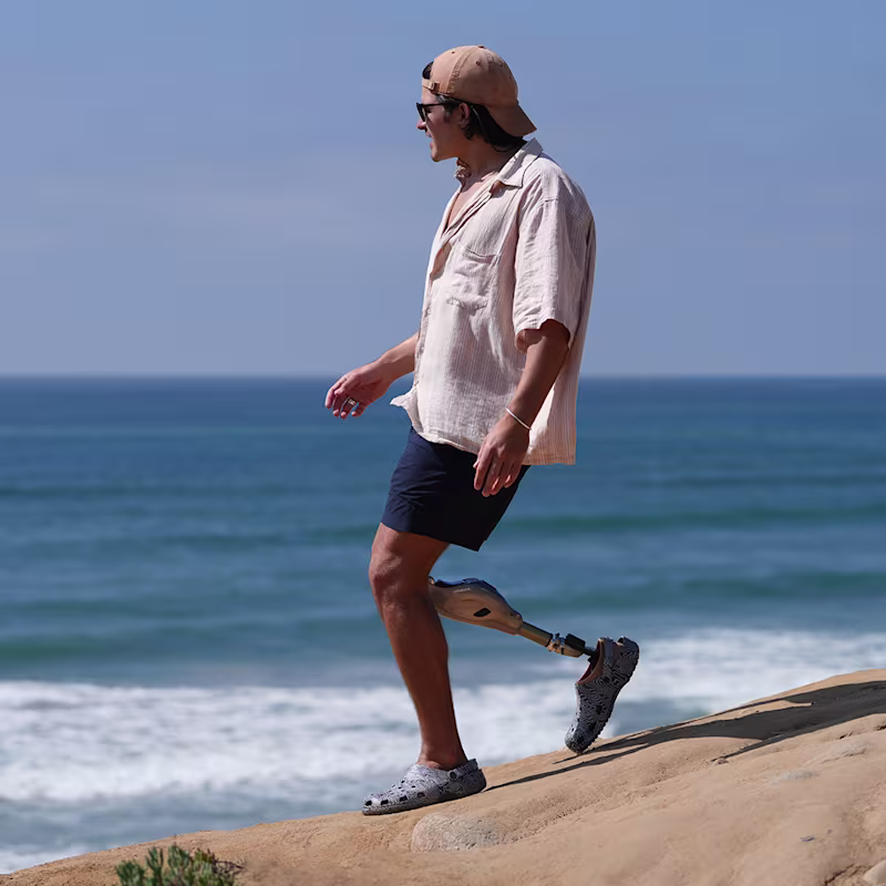 A man with a Genium X4 prosthetic knee from Ottobock is walking down a shallow rocky slope towards the sea.