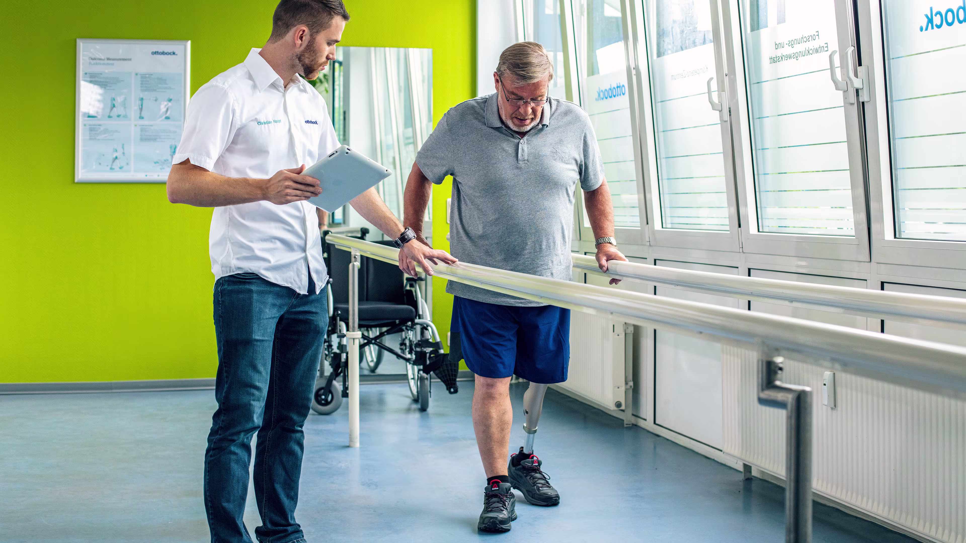 Leg amputee with Ottobock Kenevo microprocessor knee at gait training getting instructions from a prosthetist holding a tablet
