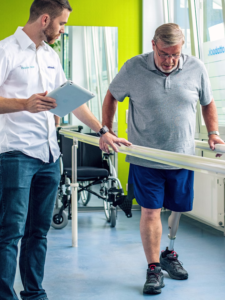 Leg amputee with Ottobock Kenevo microprocessor knee at gait training getting instructions from a prosthetist holding a tablet