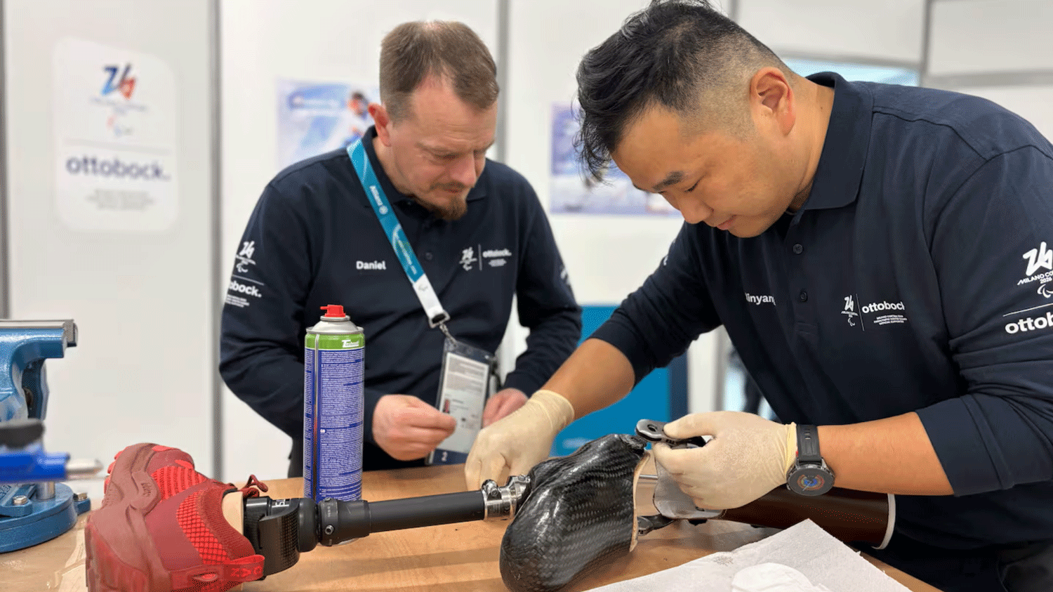 Two men in a clinical indoor setting examining and repairing a prosthetic leg
