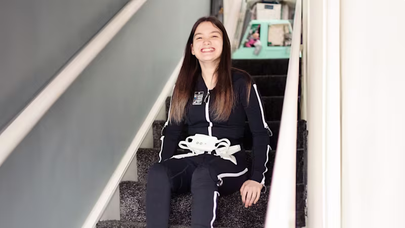 Pacient s detskou mozgovou obrnou má na sebe Ottobock's Exopulse Molii Suit a sedí na schodoch