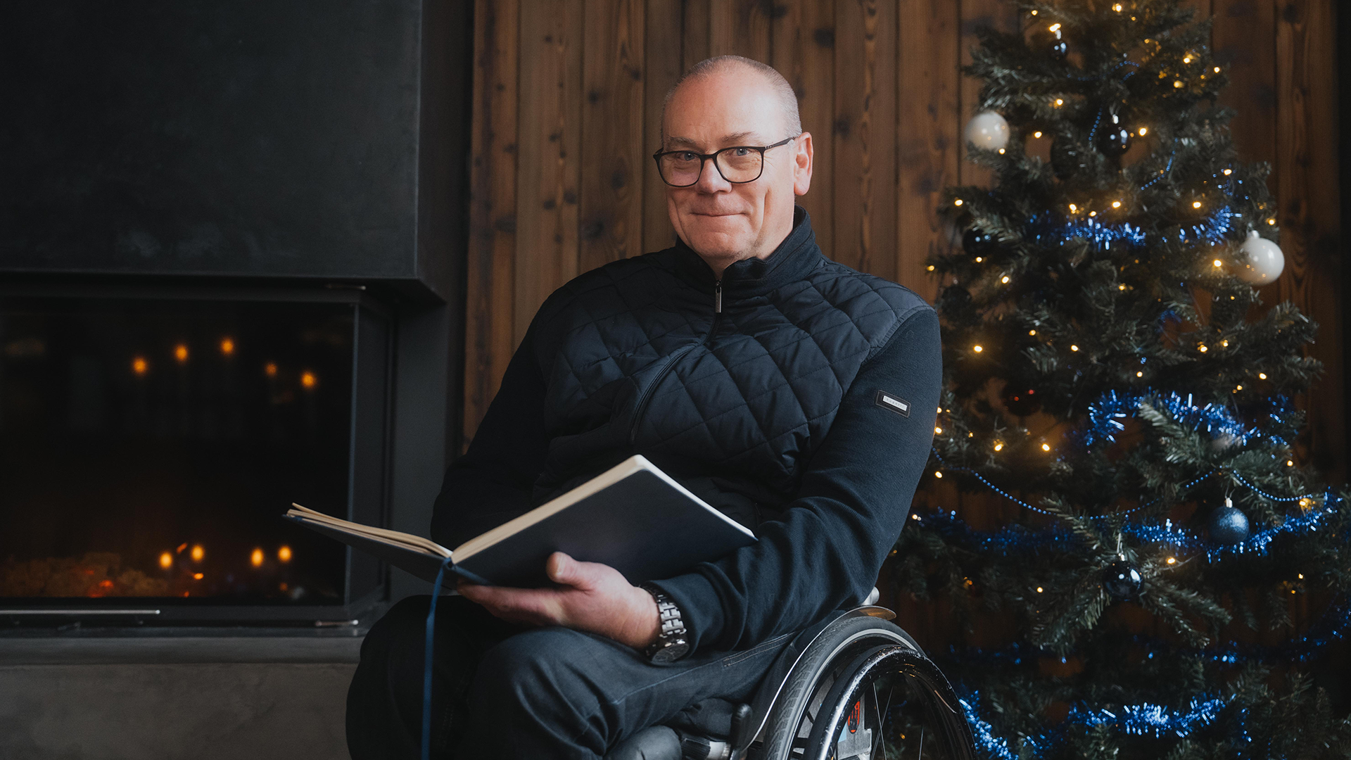 Ein Rollstuhlfahrer liest vor einem Weihnachtsbaum aus einem Buch vor.