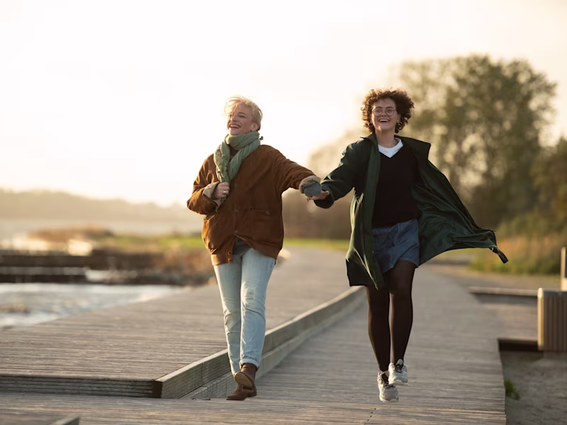 Handprothesenträgerin Lina geht mit ihrer Mutter auf einem Steg am Wasser spazieren.