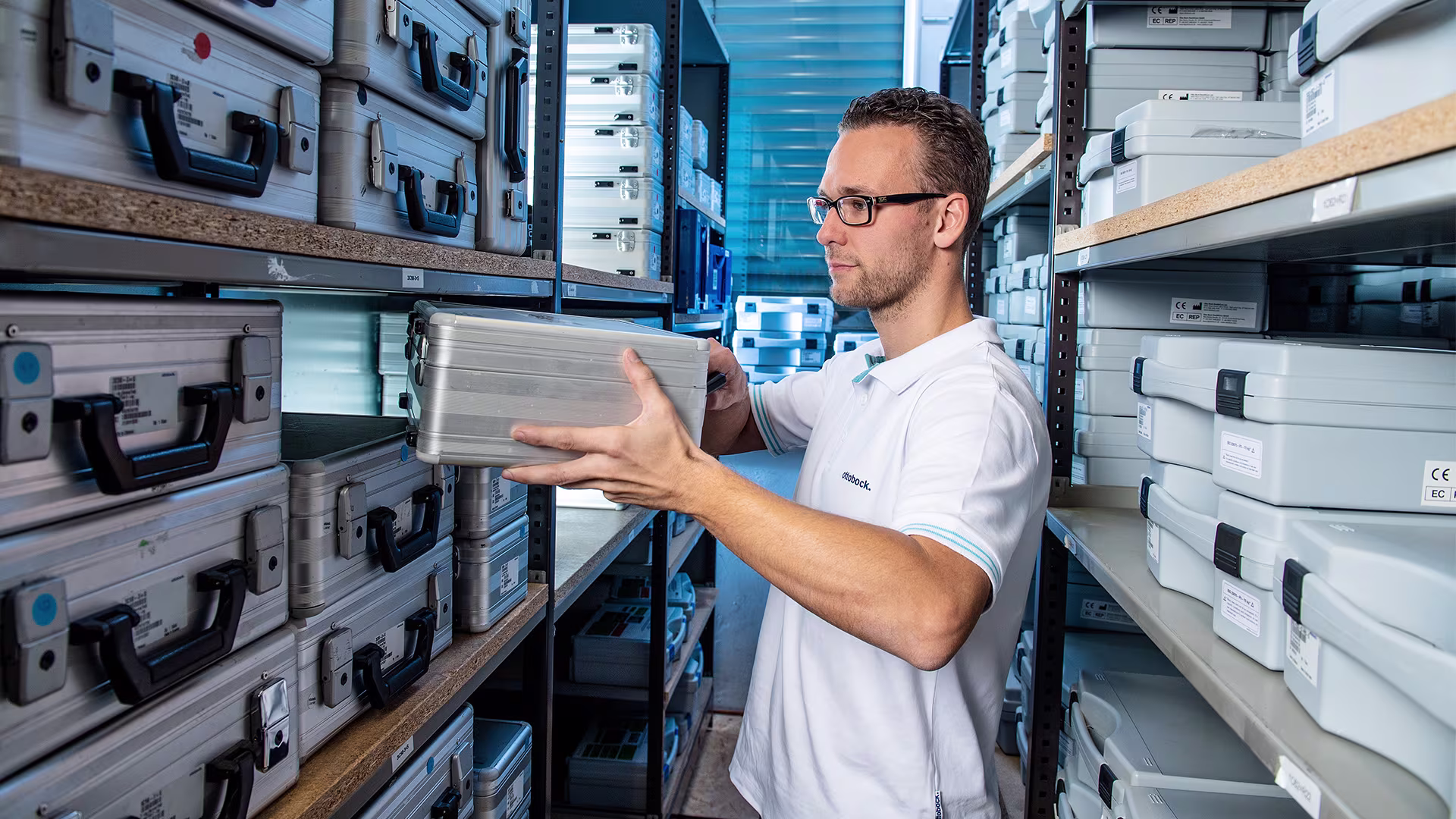 Ottobock staff member handling labeled metallic cases in organized storage facility.