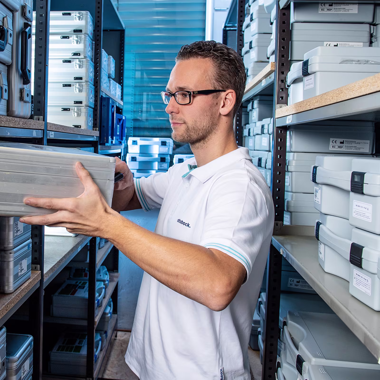 Ottobock staff member handling labeled metallic cases in organized storage facility.
